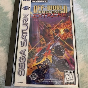 以下が含まれることがあります： 「Off-World Interceptor Extreme」のSEGA Saturnゲームケース。カバーアートは、未来的な乗り物、大きな石の頭、そして激しい爆発を描いています。ケースは透明なプラスチック製のスリーブに入っています。
