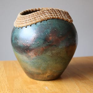 May include: A ceramic vase with a green and copper glaze, featuring a woven straw rim.