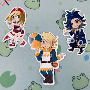 May include: Three anime-style character stickers. One sticker features a blonde character in a red and white outfit. Another shows a blonde character in a blue and white outfit holding a hat. The third sticker is of a character with blue hair.