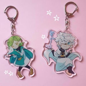 May include: Two acrylic keyrings with anime-style character designs. One character has green hair and a teal outfit, holding a blue object. The other has white hair and a white and blue outfit, holding a wand. Both have silver key rings.