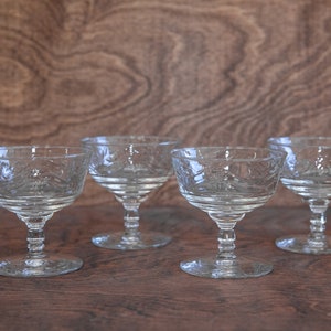 May include: Five clear glass stemmed dessert dishes with a cut glass design. The dishes are arranged in a row on a wooden surface.