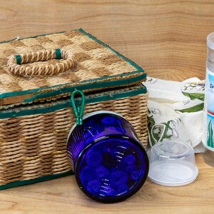 May include: A wicker basket with a green trim and a woven handle, a blue glass jar with a white lid, a clear plastic storage container with a white label that says "Storage Container", and a white plastic lid.