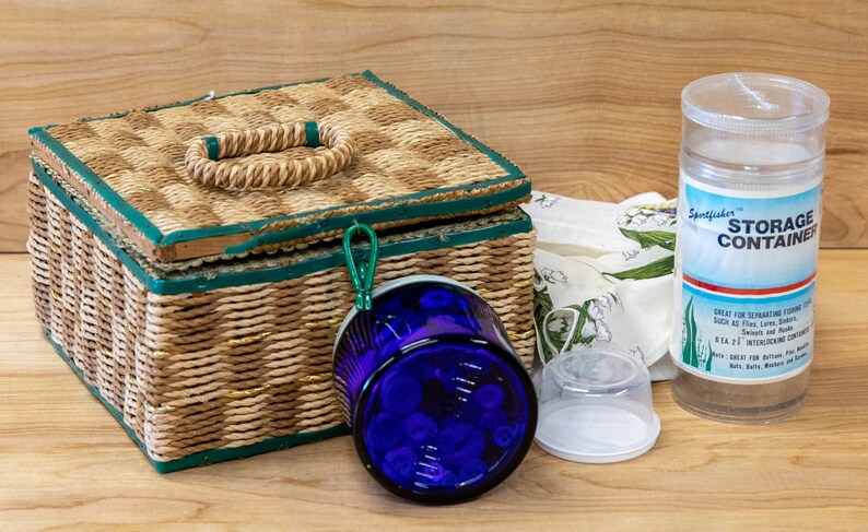 May include: A wicker basket with a green trim and a woven handle, a blue glass jar with a white lid, a clear plastic storage container with a white label that says "Storage Container", and a white plastic lid.