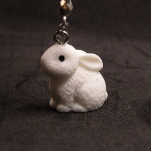 May include: A white ceramic bunny charm with a black eye, hanging from a silver chain with white and silver beads.