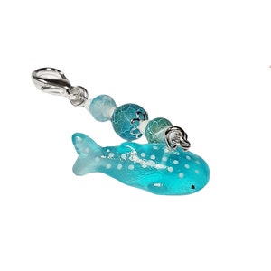 May include: A blue and white whale shark charm with white polka dots, attached to a silver chain with blue and green glass beads.