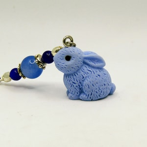 May include: A light blue bunny charm with a silver chain and blue and white beads. The bunny has a textured surface and a black eye.
