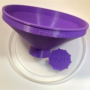 May include: A purple plastic funnel with a wide top and a narrow spout. The funnel has the text "FUNL RVAF-1.0" printed on the side. A smaller purple plastic cap with the text "FUNL LLC RVAF-1.0" is sitting on a clear plastic surface.