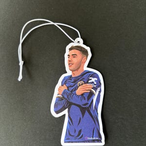 May include: A blue and white car air freshener featuring a cartoon illustration of a soccer player with his arms crossed. The text "fresh.af.co" is at the bottom of the image.