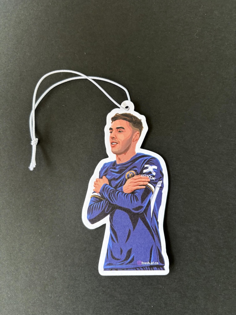 May include: A blue and white car air freshener featuring a cartoon illustration of a soccer player with his arms crossed. The text "fresh.af.co" is at the bottom of the image.