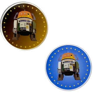 Op de afbeelding: Twee ronde, metalen, pinback-knoppen met een cartoonafbeelding van een robot. De robot is oranje, wit en groen. Eén knop heeft een gouden achtergrond met een ring van gele sterren. De andere knop heeft een blauwe achtergrond met een ring van gele sterren.