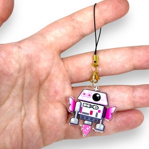 Op de afbeelding: Een roze en witte robot met vleugels en een glinsterende staartbedel. De robot is bevestigd aan een zwart touwtje met een gouden sluiting.