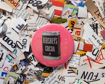 Könnte beinhalten: Ein rosa Knopf mit einem weißen und schwarzen Bild einer Dose Hershey's Cocoa. Der Knopf ist von bunten Papierschnipseln mit Text umgeben.
