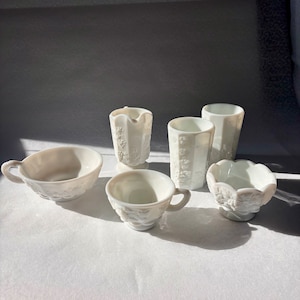 Può includere: Set di sei tazze e ciotole in vetro di latte bianco con un motivo floreale in rilievo. Le tazze e le ciotole sono tutte di dimensioni e forme diverse.