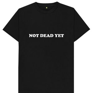 Puede incluir: Camiseta negra con texto blanco que dice "NOT DEAD YET".