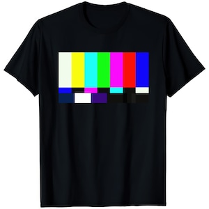 May include: Black t-shirt with a colourful test card design. The graphic shows vertical bars of white, yellow, cyan, green, magenta, red, and blue. The shirt has a crew neck.