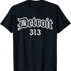 Puede incluir: Camiseta negra con la palabra "Detroit" en blanco, con una fuente estilizada y contorno blanco. Debajo de la palabra "Detroit" está el número "313" en blanco, una referencia al código de área de la ciudad.