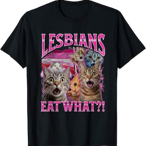 May include: Black t-shirt with a graphic of several cats with surprised expressions. The text "LESBIANS" arches above the cats, with "EAT WHAT?!" below, all in pink. A pink and white flag is in the background.