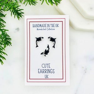 May include: A set of three cute mismatched earrings featuring black and white orca designs. The earrings are handmade in the UK. The card reads "Handmade in the UK Mismatched Collection Cute Earrings UK".