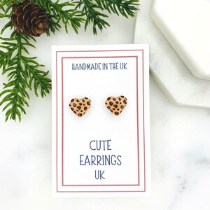 May include: A pair of heart-shaped stud earrings with a leopard print design. The earrings are displayed on a white card with the text "Handmade in the UK" and "Cute Earrings UK".