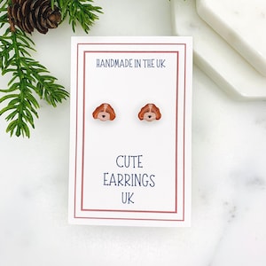 May include: A pair of small, brown and white dog face stud earrings on a white card with the text "HANDMADE IN THE UK" and "CUTE EARRINGS UK".