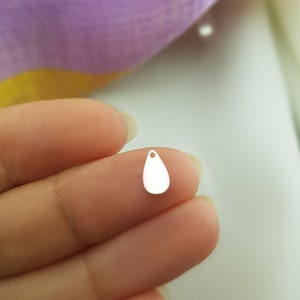 Puede incluir: Un colgante de plata en forma de lágrima con un pequeño agujero en la parte superior para enhebrar.