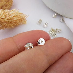 May include: Close-up of several small, shiny silver earring backs. One back is in focus, displaying the "925" hallmark, indicating sterling silver. The backs are scattered, suggesting a collection or supply of jewelry components.