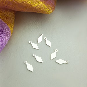 May include: Ten silver-colored diamond-shaped charms with a small loop at the top. The charms are arranged in a semi-circle on a light gray surface.