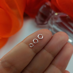 May include: Four silver jump rings of different sizes, displayed on a finger.