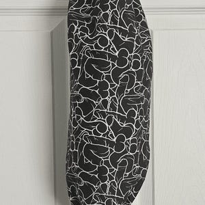 May include: A black and white patterned bag, hanging from a white hook. The bag features a repeating design of abstract shapes. The bag is made of fabric and has a drawstring closure at the bottom.