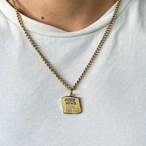 May include: A gold chain necklace with a gold pendant shaped like a newspaper with the words "GOOD NEWS" printed on it.