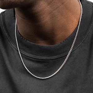 Könnte beinhalten: Eine silberne Halskette mit einem filigranen Perlendesign. Die Halskette wird über einem schwarzen Rundhals-Shirt getragen. Die Kette ist ein schlichtes, elegantes Accessoire.
