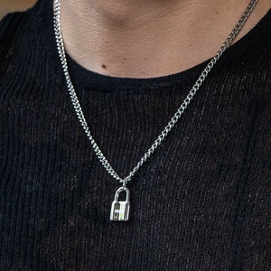 Könnte beinhalten: Eine silberne Kettenkette mit einem kleinen Schlossanhänger.