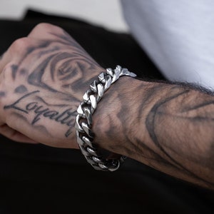 Könnte beinhalten: Ein silbernes Curb-Kettenarmband mit einem großen, klobigen Gliederdesign.