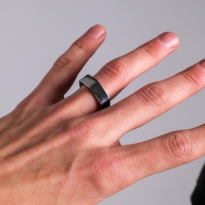 Könnte beinhalten: Ein silberner Bandring mit quadratischer Form.