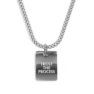 Könnte beinhalten: Eine silberne Kettenkette mit einem rechteckigen Anhänger, auf dem "TRUST THE PROCESS" steht.