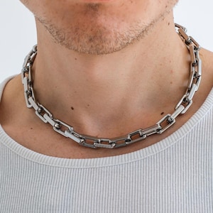 Könnte beinhalten: Eine silberne Kettenkette mit einem Box-Ketten-Design. Die Kette ist dick und hat einen klobigen Look.