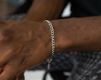 May include: A silver curb chain bracelet on a person's wrist.
