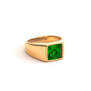 Könnte beinhalten: Ein goldfarbener Ring mit einem quadratischen, smaragdgrünen Edelstein. Der Ring hat ein dickes Band und eine rechteckige Fassung für den leuchtend grünen Stein. Der Ring ist vor einem weißen Hintergrund platziert.