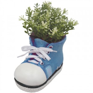 May include: A blue ceramic sneaker-shaped planter filled with green and white faux plants. The planter has white laces, a white toe, and a black sole. A decorative item for home or office.