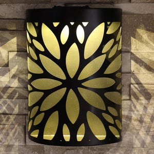 May include: Black metal solar powered wall light with a cut-out design of leaves and a warm white light shining through.