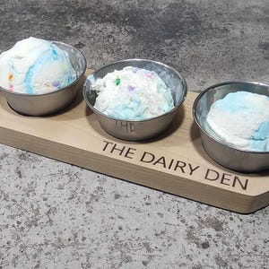 May include: Four small metal bowls filled with ice cream on a wooden serving tray. The tray is engraved with the words "The Dairy Den".