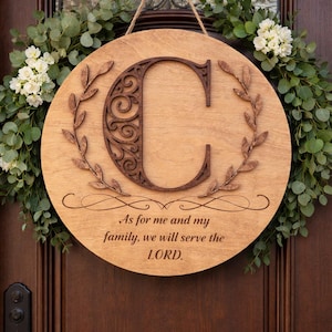May include: Wooden round sign with a large, ornate letter "C" and the inscription "As for me and my family, we will serve the LORD." The sign is surrounded by a green and white floral wreath and hangs on a wooden door.