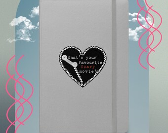 Pode incluir: Um caderno cinza com um remendo preto em forma de coração que diz "What's your favourite Scary movie?" em texto branco com um gráfico de controlador de videogame branco dentro do coração.