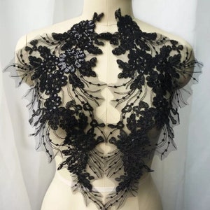May include: Black lace applique with floral and sequin details. The applique features intricate designs and is likely used for embellishing garments or accessories. The delicate lace is set against a sheer background, creating a layered effect.