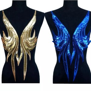 May include: Two sequined wing appliques, one gold and one blue, displayed on black mannequins. The gold wing has a gradient effect, while the blue wing sparkles. These decorative appliques are ideal for costumes or embellishments.