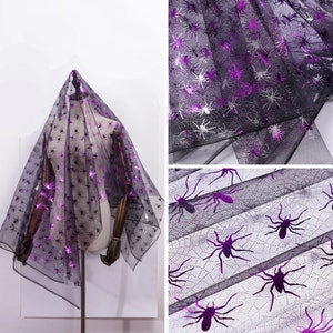 May include: Black sheer fabric featuring a spider web design with metallic purple spider accents. The fabric is draped over a mannequin. Suitable for Halloween or themed crafts. The fabric is see-through.