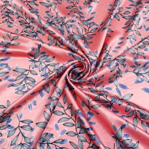 May include: A swirled, silky fabric with a pink background and a repeating pattern of stylized leaves. The leaves are primarily gray with blue accents and black outlines, creating a botanical design. The fabric has a glossy sheen.