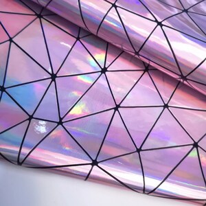 May include: Holographic pink vinyl sheet with a geometric triangular pattern. The vinyl reflects a rainbow of colours, with black lines defining the shapes. The material is folded, showing its flexibility and texture. Suitable for crafts and DIY projects.
