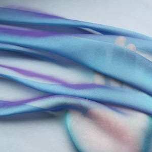 May include: A flowing, sheer fabric in shades of light blue and purple. The fabric has a soft, rippled texture, with the colors blending and creating a watercolor effect. The overall look is delicate and ethereal.