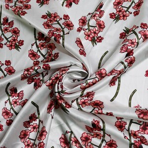 K&ouml;nnte beinhalten: Wei&szlig;er Satin-Stoff mit einem sich wiederholenden Muster aus roten und rosa Kirschbl&uuml;tenzweigen. Der Stoff ist drapiert und zeigt den Glanz und die Textur des Materials. Das florale Design ist detailliert und lebendig.